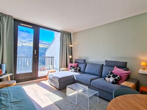 A modern living room with a grey sofa, a clear coffee table, a wooden side table, and a view of a snowy landscape through a sliding door.