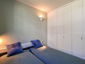 Un dormitorio con dos camas, un armario y una lámpara de noche.