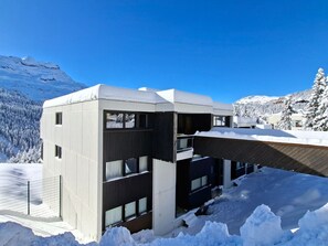 Un edificio moderno con techo plano, grandes ventanales y un paisaje nevado al fondo.