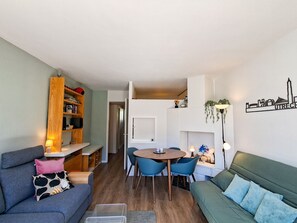Un espacio habitable funcional con sofá, una mesa de comedor con sillas, estantería y lámpara de pared.