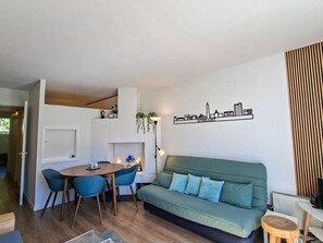 A modern living room with a green sofa, a dining table with chairs, and a cityscape wall art.