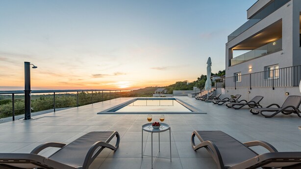 Un espace piscine aménagé sur le toit, avec des chaises longues et une table où sont servis des boissons, offrant une vue sur le coucher du soleil et un panorama lointain.