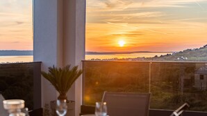 Une table à manger dressée avec des assiettes, des verres et une bougie, offrant une vue sur un coucher de soleil.