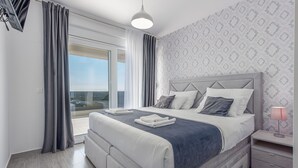 Une chambre à coucher moderne avec un grand lit, une table de chevet, une lampe et une vue sur l’extérieur.