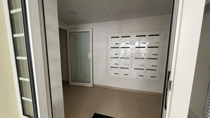 En hall med ett kaklat golv, en svart dörrmatta och en rad vita skåp längs väggen.