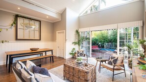 Un salón amplio con una gran mesa de madera, un sofá cómodo y vistas a un jardín exuberante a través de amplios ventanales.