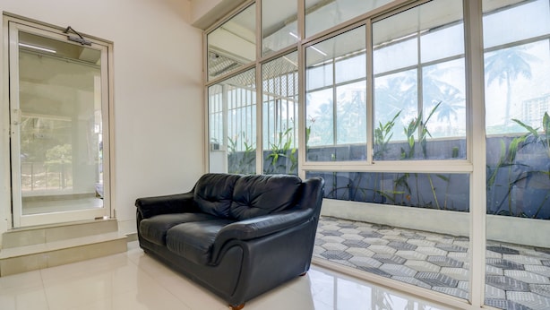 A spacious room with a black leather sofa, large windows with a view of greenery, and a tiled floor. - Itsy Hotels Ushodaya Royal Residency (Thiruvananthapuram)