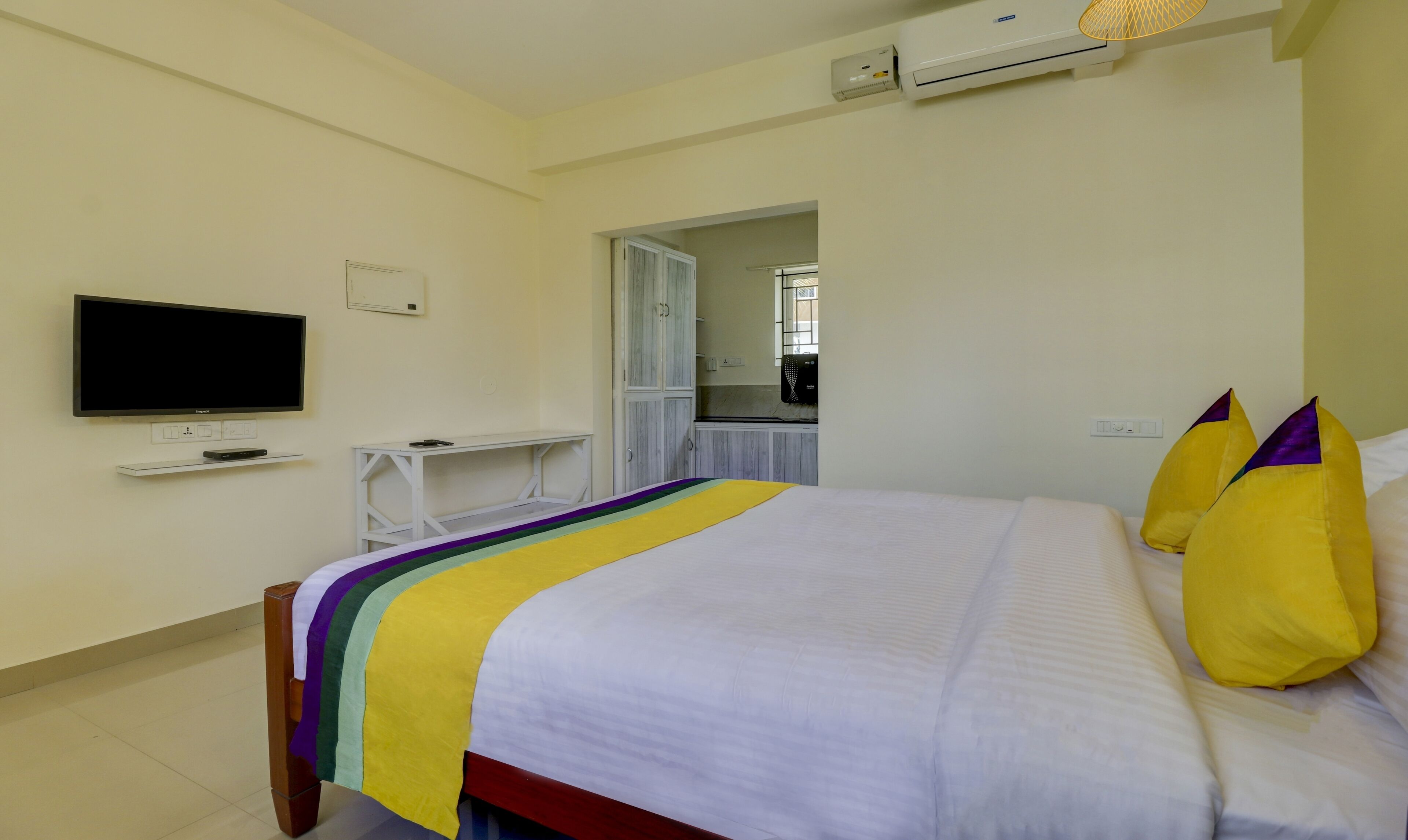 A hotel room with a bed, a TV, a desk, and an air conditioning unit.