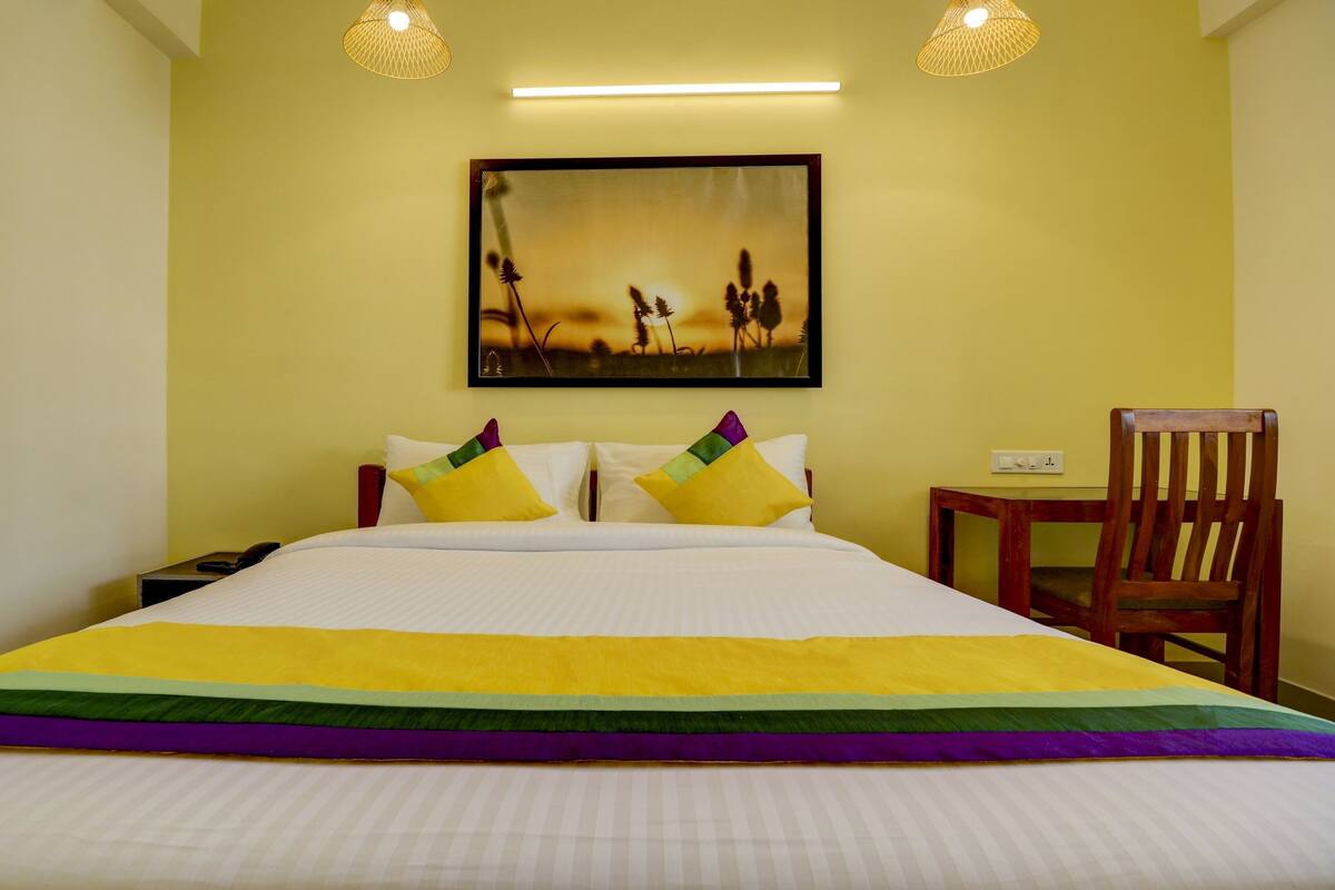 Una habitación de hotel con cama, mesita de noche, una silla y un cuadro en la pared.
