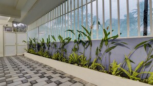 A corridor with a tiled floor, a wall with vertical blinds, and a row of green plants. - Itsy Hotels Ushodaya Royal Residency (Thiruvananthapuram)
