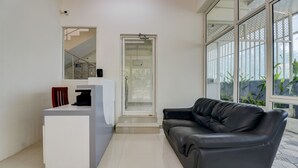 A modern reception area with a reception desk, a black leather couch, and a glass door leading to a staircase. - Itsy Hotels Ushodaya Royal Residency (Thiruvananthapuram)