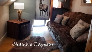 A cozy room with a wooden floor, a dark brown sofa with patterned cushions, a small wooden side table with a lamp, a large wall painting of a deer, and a shelf with decorative items. - Comfort 2-room, 6 ppl, Terrace & Garden in Valloire (Valloire)