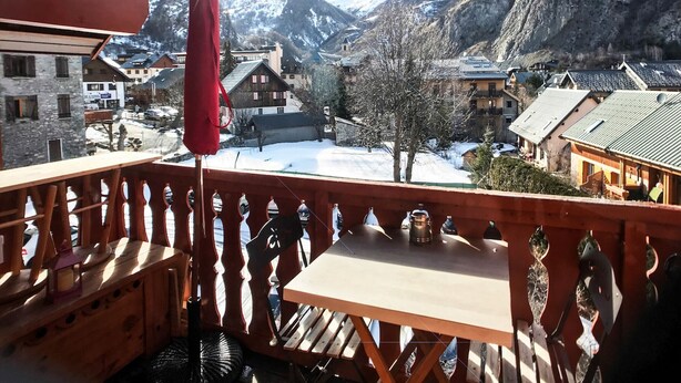 A wooden balcony with a table and chairs, overlooking a snowy village with traditional buildings and mountains in the background. - Studio cabin + mezzanine for 4, West-facing balcony in Valloire (Valloire)