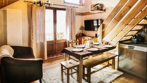 A cozy dining area with a wooden table set for four, a chandelier, and a television above the table. - Studio cabin + mezzanine for 4, West-facing balcony in Valloire (Valloire)