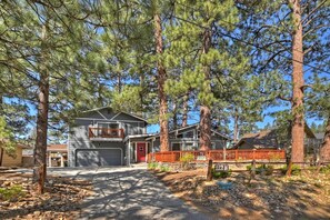A two-story house with a garage, surrounded by tall pine trees.