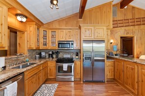 A spacious kitchen with wooden cabinets, stainless steel appliances, granite countertops, and a patterned rug.