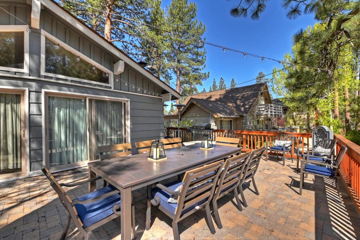 Une terrasse avec une table et des chaises en bois, un barbecue et une plateforme avec une rambarde.