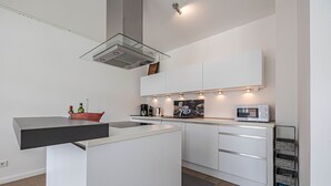 Une cuisine moderne avec des meubles blancs, un four à micro-ondes encastré et une hotte de cuisinière en verre.