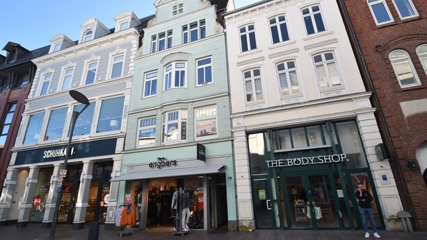 A row of historic buildings with storefronts, including a body shop and a clothing store.