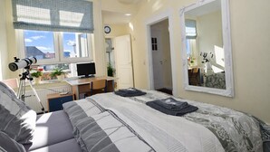 A bedroom with a bed, a desk with a computer, a telescope, and a large mirror.
