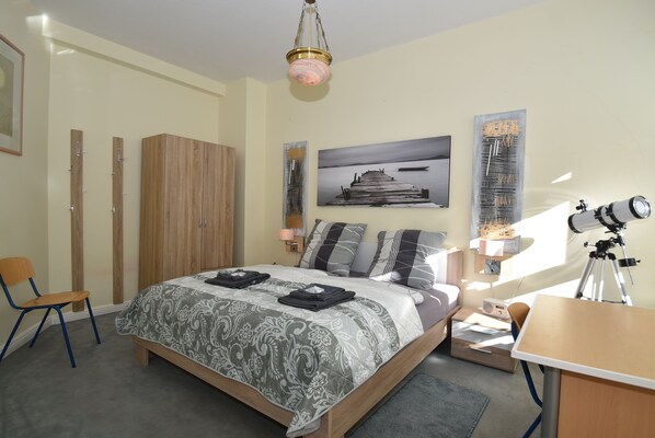 A bedroom with a bed, a desk, a chair, a wardrobe, and a telescope.