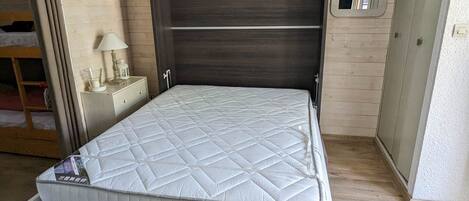 Un dormitorio compacto con una cama individual, una mesita de noche con lámpara y un estante pequeño.
