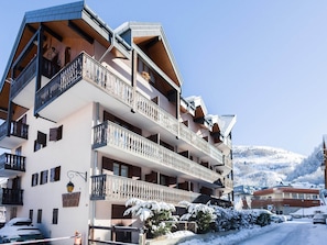 A multi-story hotel with balconies, a sign indicating 'RESIDENCE LE TIGNY,' and a snowy mountain backdrop.