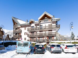 A multi-story hotel with balconies, a parking area with snow-covered cars, and a mountainous backdrop. - 2-room cabin south apartment in Valloire, 4 pers, pets allowed (Valloire)