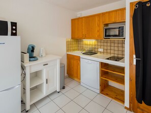 Una cocina funcional con armarios de madera, microondas, lavavajillas y encimera blanca.