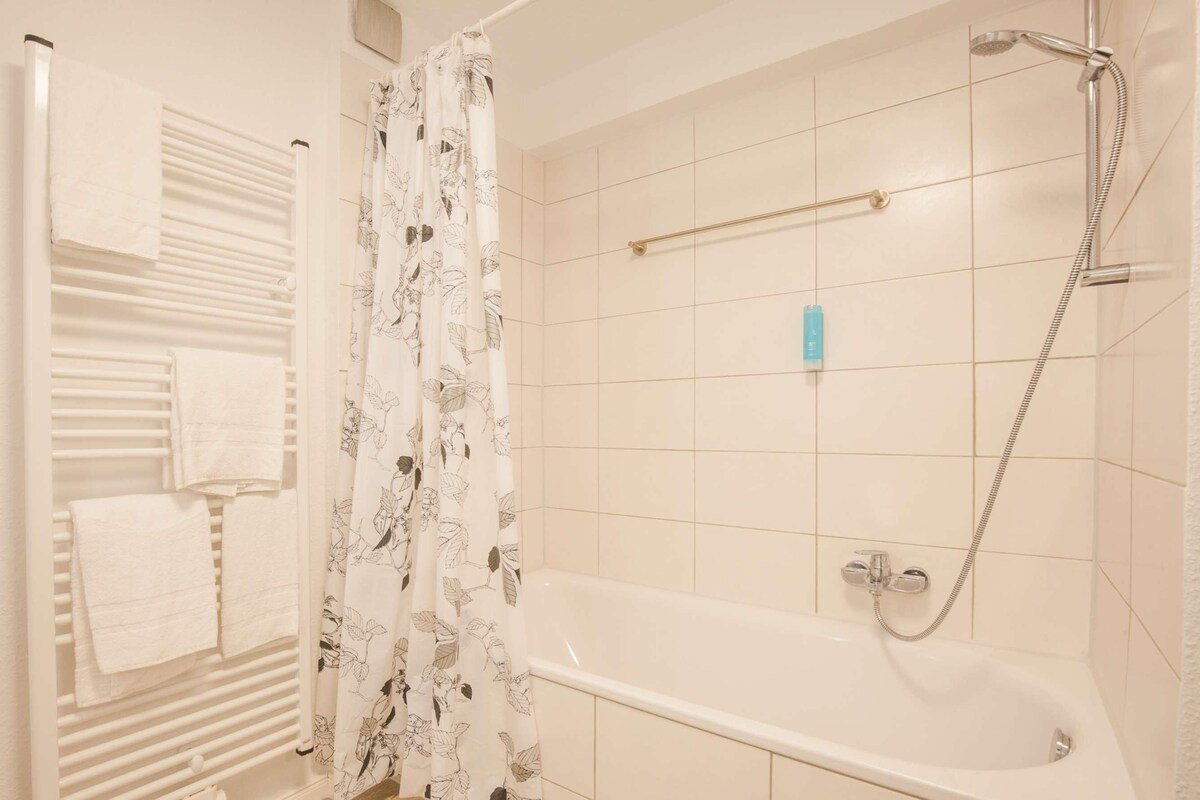 A bathroom with a bathtub, a shower, and a towel rack with towels.