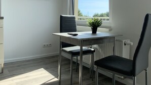 A modern, well-lit room with a dining table, two chairs, a potted plant, and a TV mounted on the wall. - City Apartments Wilhelmshaven (Wilhelmshaven)