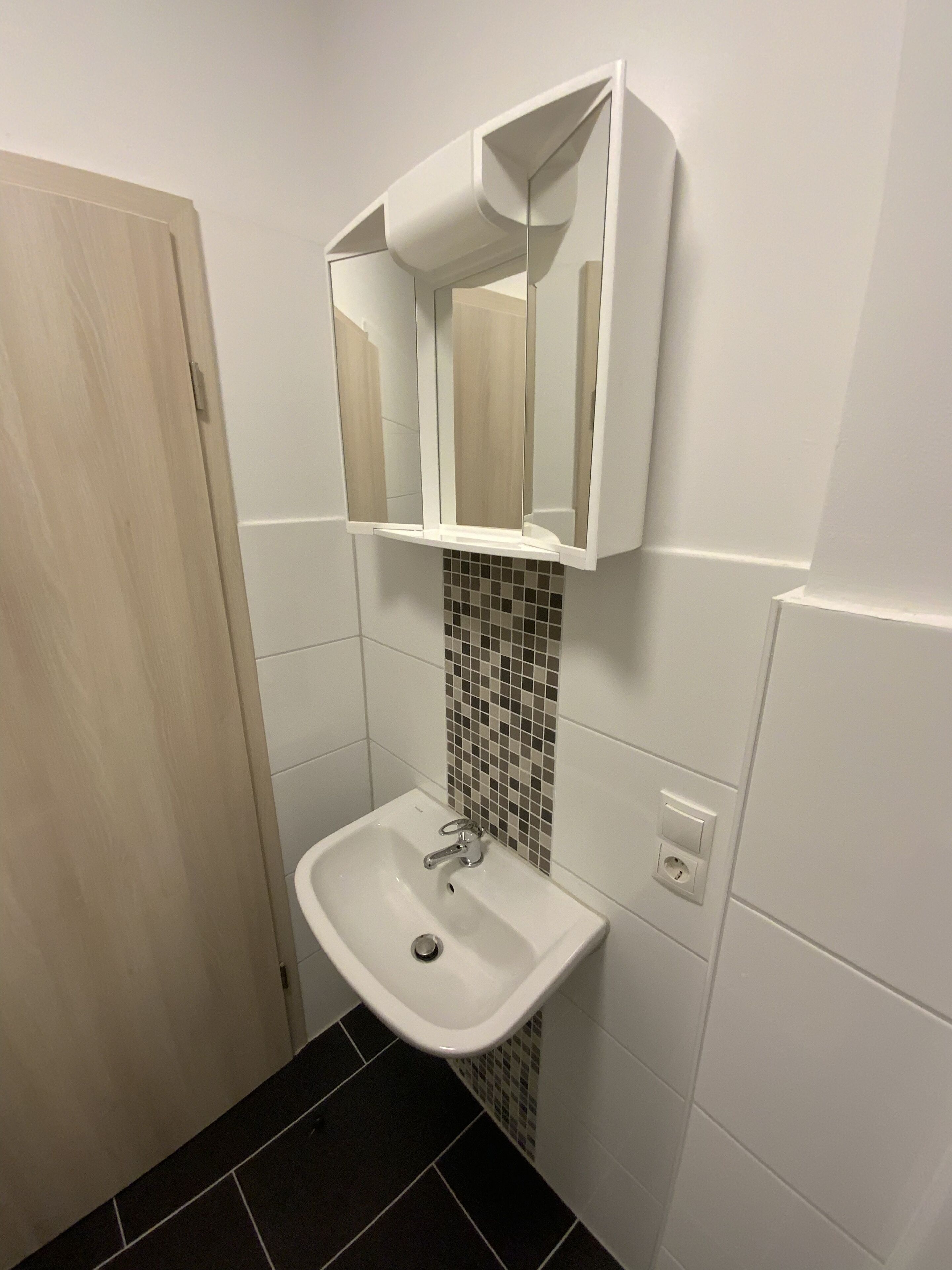 Ein Badezimmer mit einem weißen Waschbecken, einem Spiegel und einer gefliesten Rückwand.