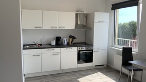 A modern kitchen with white cabinets, a black stove, and a window with a view of trees. - City Apartments Wilhelmshaven (Wilhelmshaven)