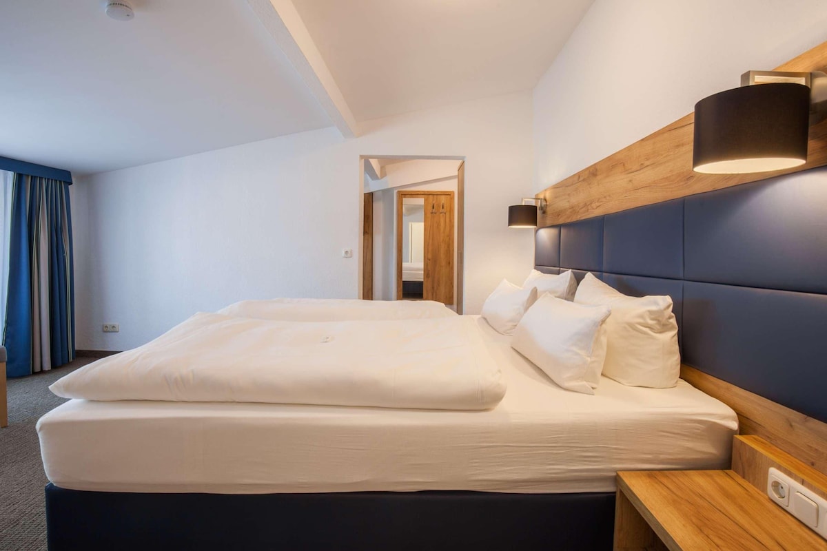A hotel room with a large bed, a wooden headboard, a bedside table, and a mirror.