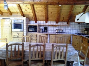 Una cocina rústica con armarios de madera, salpicadero de azulejos y una mesa de comedor de madera con sillas.