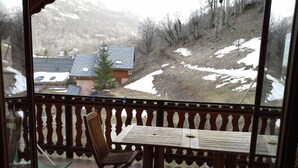 A balcony with a wooden table and chair, overlooking a snowy landscape with houses and trees.