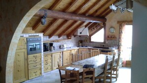 A rustic kitchen with wooden cabinets, a large wooden dining table, and a vaulted ceiling.