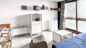 A compact room with a bed, a desk, a chair, a small cabinet, and a television.