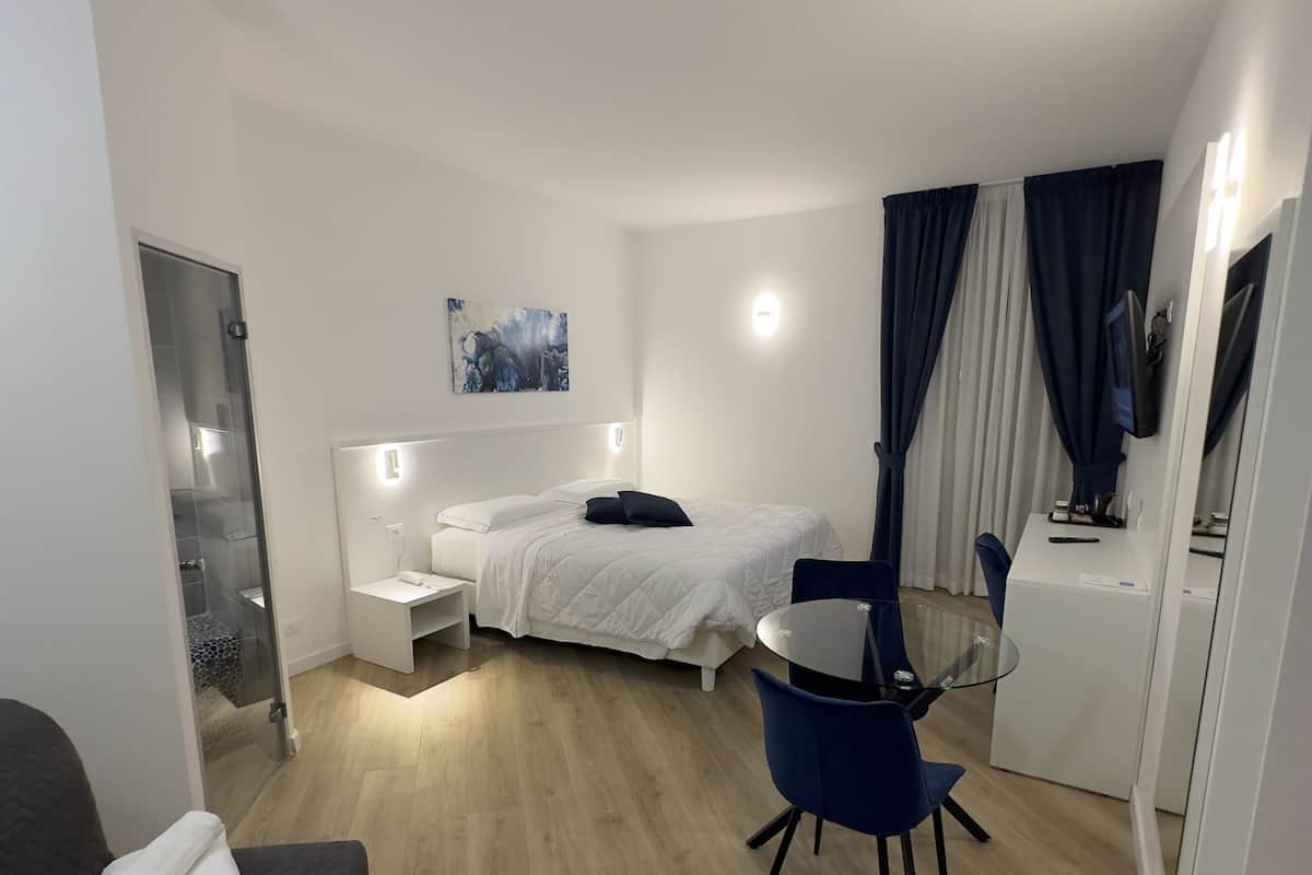 A modern hotel room with a bed, bedside table, and a small desk with a chair.
