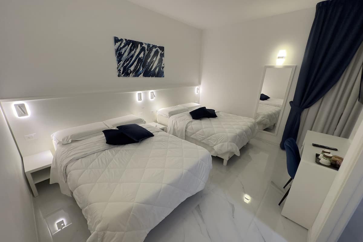 A hotel room with two beds, white bedding, a marble floor, a painting on the wall, and a mirror.