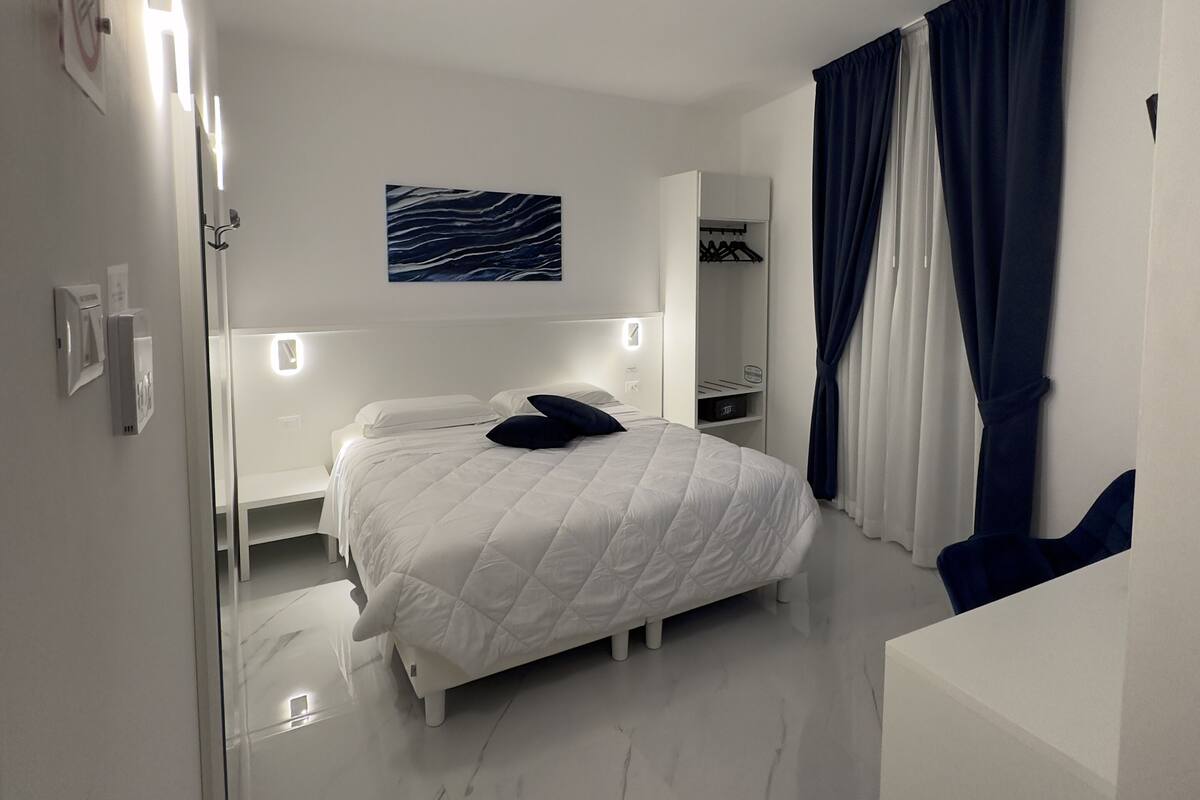 A modern bedroom with a white bed, a nightstand, a mirror, and a wardrobe.
