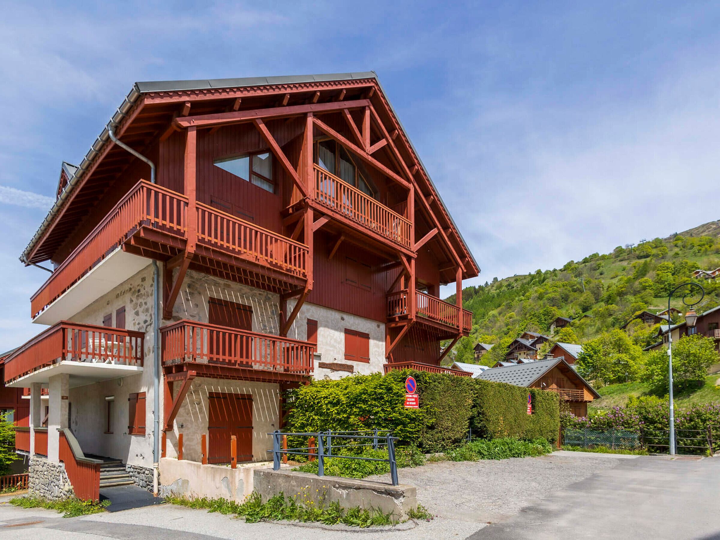 Un chalet à plusieurs étages, doté de balcons, d’une base en pierre et entouré d’une colline.