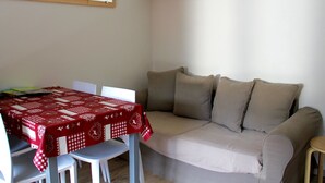 A small, well-lit room with a red and white checkered tablecloth, a beige sofa, and a white wall-mounted shelf with a kettle and a mug. - 2-room cabin apartment for 4 people, west facing with balcony and collective parking (Valloire)