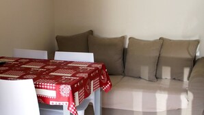 A room with a dining table covered with a red tablecloth, a sofa with beige cushions, and a white chair. - 2-room cabin apartment for 4 people, west facing with balcony and collective parking (Valloire)