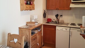 Cocina compacta con armarios de madera, microondas, lavavajillas y cafetera.