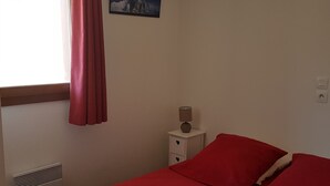 Un dormitorio con cama, mesita de noche, lámpara, ventana con cortinas y un cuadro colgado en la pared.