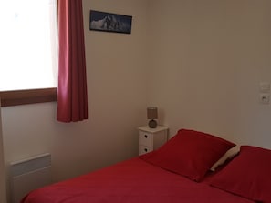 Quarto com cama, mesa de cabeceira, luminária, janela com cortinas e um quadro na parede.