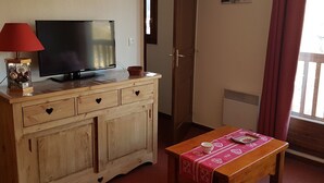 Una habitación con un armario de madera, un televisor, una mesa roja cubierta con un mantel y una puerta que da a otra habitación.