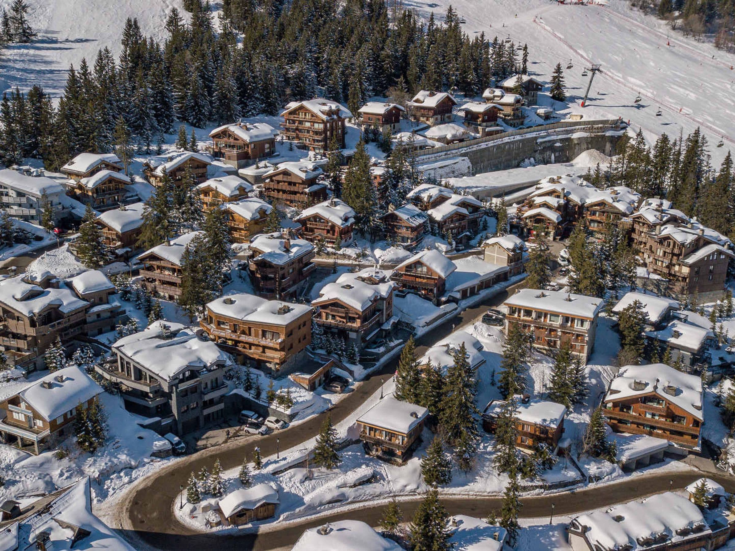A snow-covered resort with multiple wooden buildings, a ski lift, and a winding road.