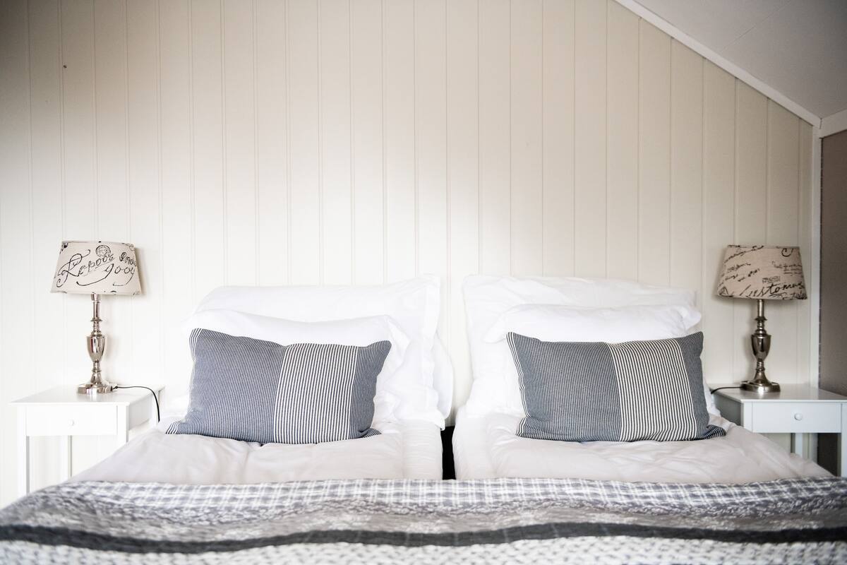 A neatly made bed with white linens and striped pillows, flanked by two bedside tables with lamps.